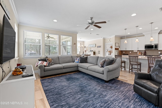 living room with ceiling fan with notable chandelier, wood-type flooring, and crown molding