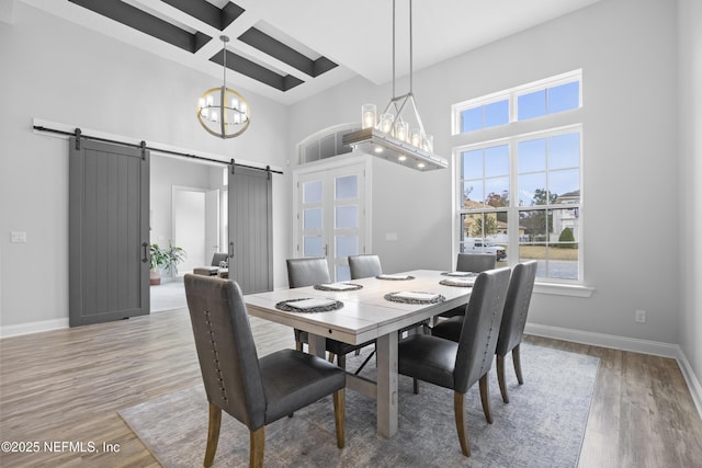 dining space featuring hardwood / wood-style floors, beamed ceiling, a notable chandelier, a barn door, and coffered ceiling