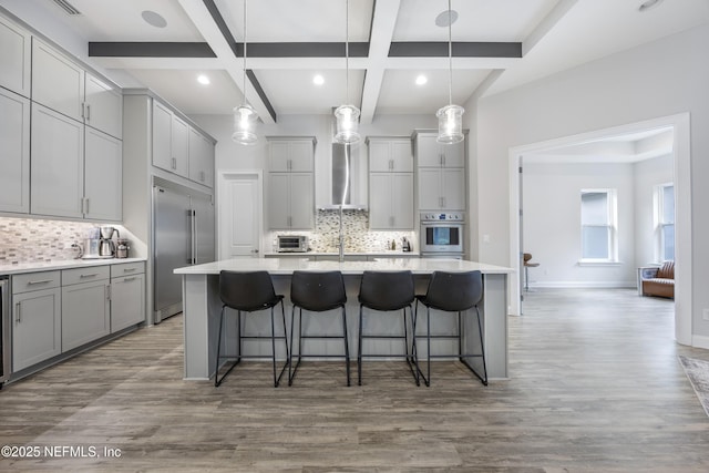 kitchen featuring built in fridge, pendant lighting, wood-type flooring, and an island with sink