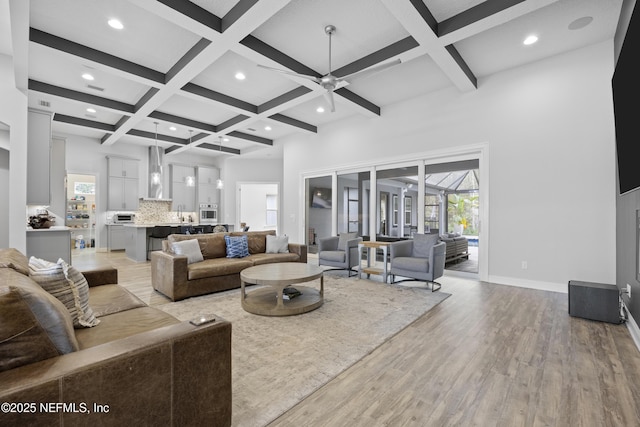 living room with ceiling fan, a towering ceiling, beam ceiling, coffered ceiling, and light hardwood / wood-style floors