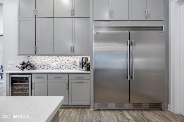 kitchen with wine cooler, stainless steel built in fridge, backsplash, gray cabinetry, and light stone counters