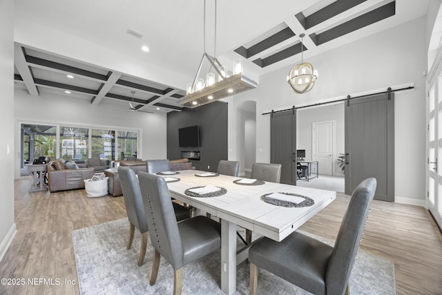 dining area with light hardwood / wood-style flooring, beam ceiling, a barn door, ceiling fan with notable chandelier, and coffered ceiling