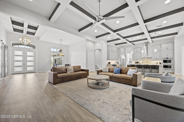 living room featuring coffered ceiling, beamed ceiling, ceiling fan with notable chandelier, and light hardwood / wood-style flooring