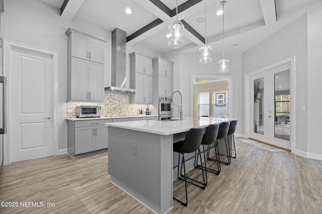 kitchen with hanging light fixtures, french doors, wall chimney exhaust hood, light wood-type flooring, and a center island with sink