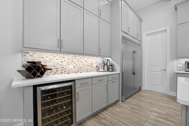 kitchen with backsplash, built in fridge, beverage cooler, and light hardwood / wood-style floors