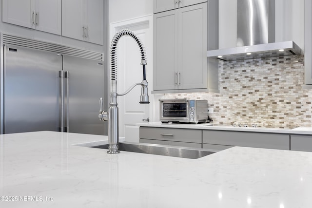 kitchen with built in fridge, light stone countertops, wall chimney exhaust hood, black electric stovetop, and decorative backsplash