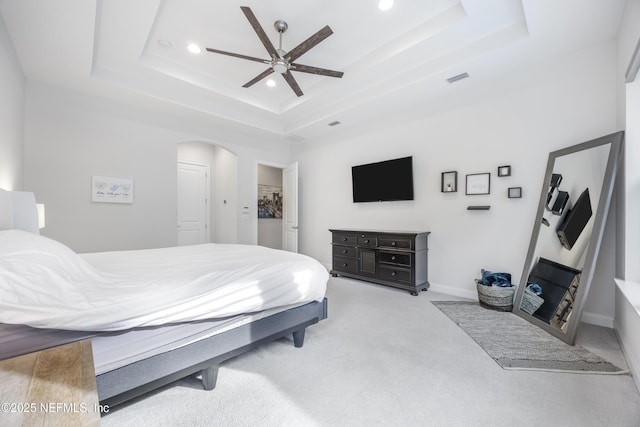 bedroom with light colored carpet, ceiling fan, and a raised ceiling