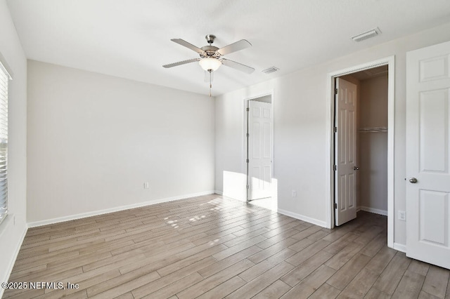 unfurnished bedroom featuring a closet, ceiling fan, light wood-type flooring, and a spacious closet