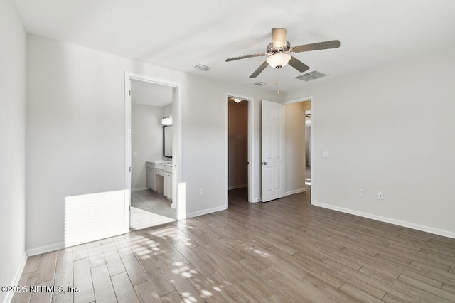 unfurnished bedroom featuring a closet, ensuite bath, light hardwood / wood-style floors, ceiling fan, and a walk in closet