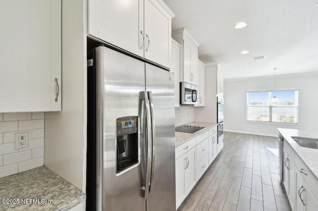 kitchen with light stone counters, decorative backsplash, crown molding, white cabinets, and appliances with stainless steel finishes