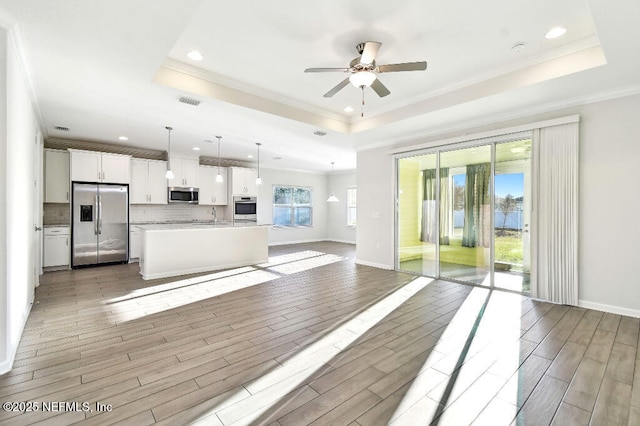 kitchen featuring white cabinets, a raised ceiling, pendant lighting, a kitchen island with sink, and appliances with stainless steel finishes