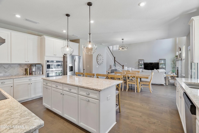 kitchen with stainless steel appliances, hanging light fixtures, a kitchen island, white cabinets, and a breakfast bar