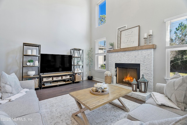 living room with a high ceiling, dark hardwood / wood-style floors, and a stone fireplace