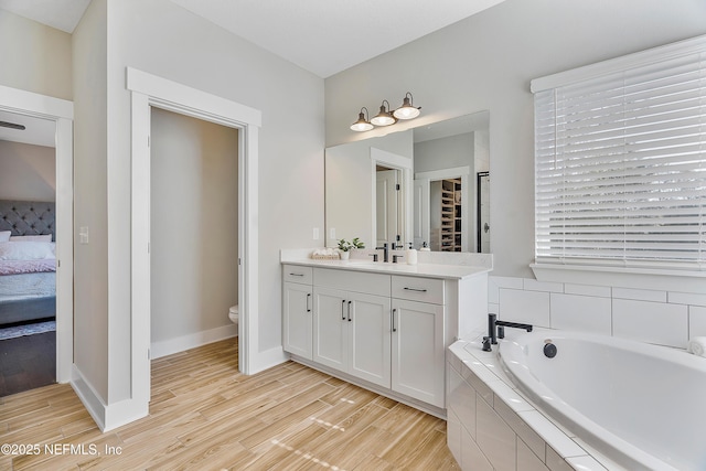 bathroom with toilet, a relaxing tiled tub, hardwood / wood-style floors, and vanity