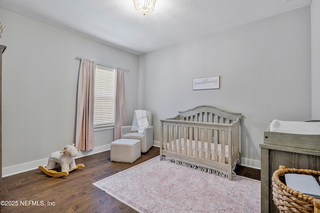 bedroom featuring a textured ceiling, a nursery area, and dark hardwood / wood-style flooring