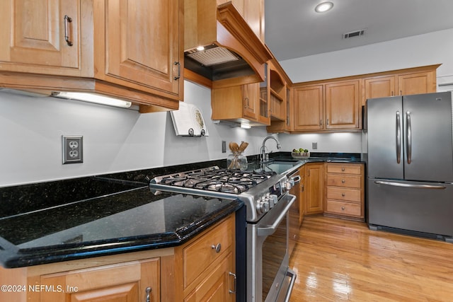 kitchen with premium range hood, dark stone counters, stainless steel appliances, sink, and light hardwood / wood-style floors