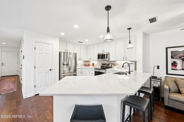 kitchen with sink, tasteful backsplash, hanging light fixtures, appliances with stainless steel finishes, and white cabinets