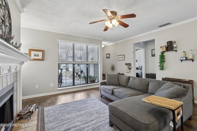 living room featuring visible vents, ornamental molding, a tile fireplace, wood finished floors, and a ceiling fan