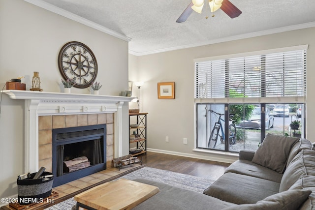 living area featuring a tiled fireplace, wood finished floors, crown molding, and a ceiling fan