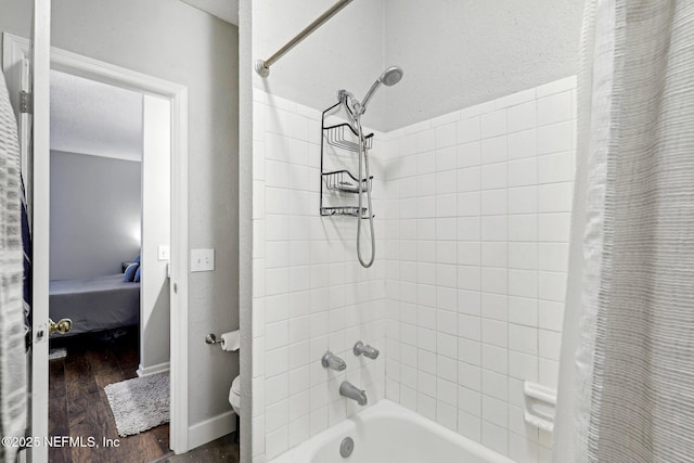 ensuite bathroom with baseboards, wood finished floors, shower / tub combo with curtain, a textured wall, and a textured ceiling