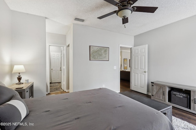 bedroom with visible vents, wood finished floors, a textured ceiling, ensuite bath, and a ceiling fan