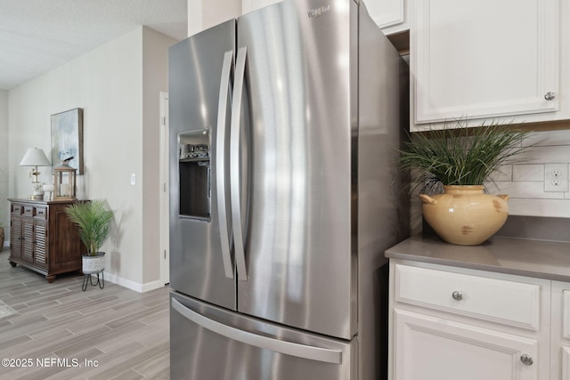 kitchen with white cabinets, stainless steel fridge, light wood-type flooring, and tasteful backsplash