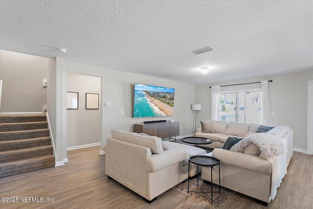 living room with visible vents, baseboards, stairs, wood finished floors, and a textured ceiling