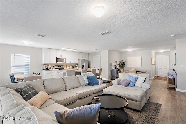 living area featuring visible vents, baseboards, a textured ceiling, and wood finished floors