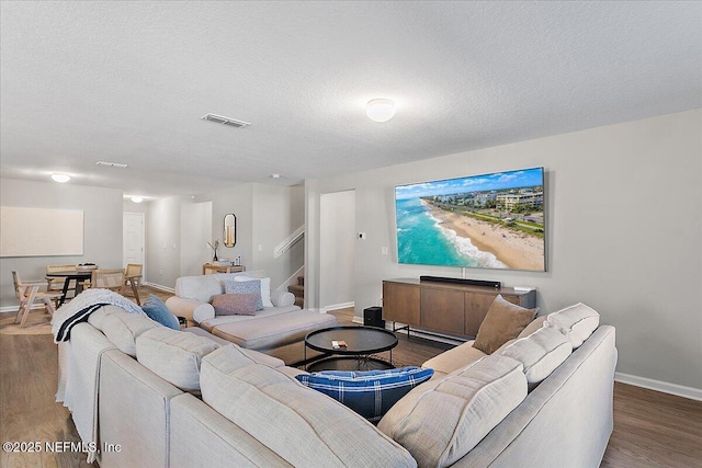 living area featuring visible vents, a textured ceiling, wood finished floors, baseboards, and stairs