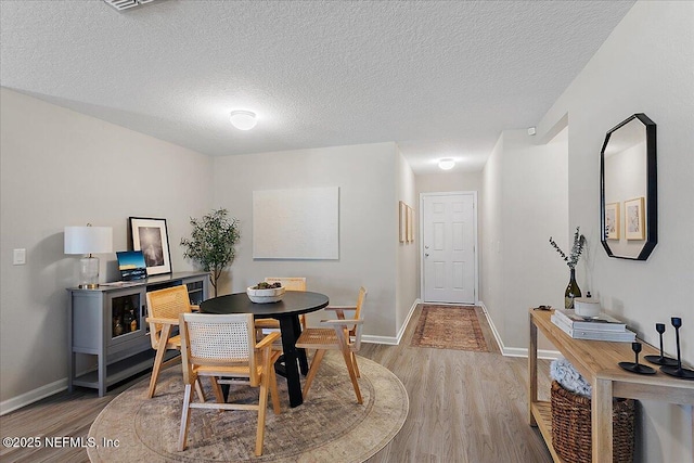 dining space featuring baseboards, a textured ceiling, and wood finished floors