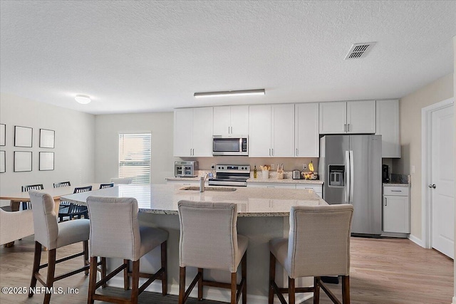 kitchen with light wood-style flooring, appliances with stainless steel finishes, a breakfast bar, and a sink