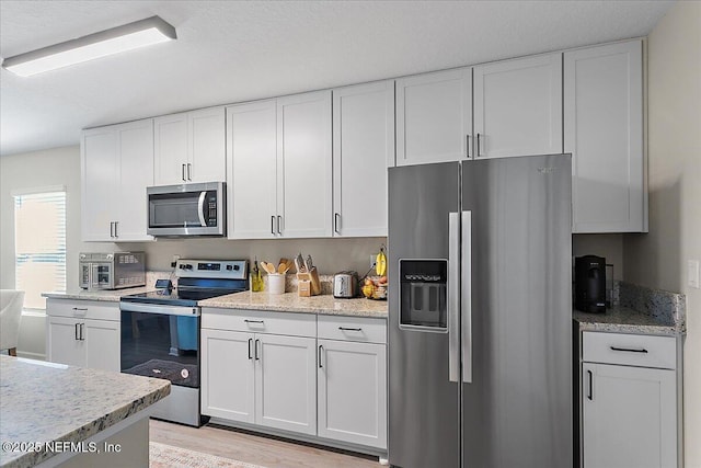 kitchen with light wood finished floors, appliances with stainless steel finishes, and white cabinetry