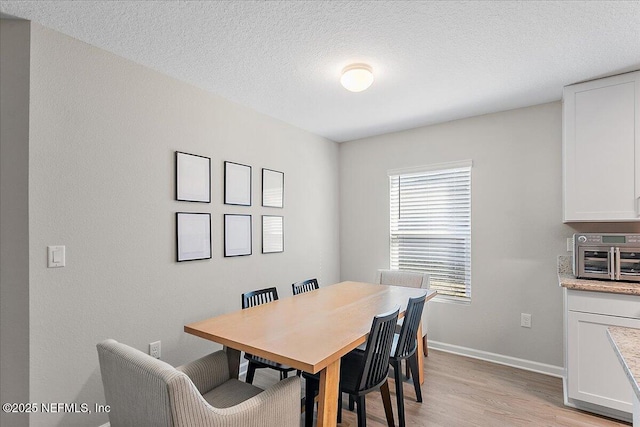 dining space featuring light wood-type flooring, baseboards, a textured ceiling, and a toaster