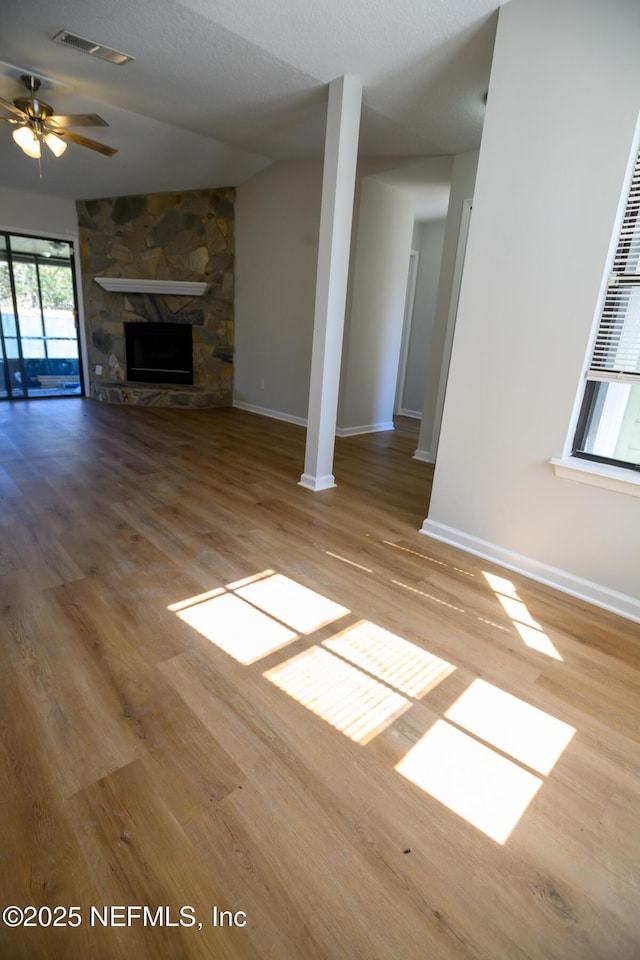 unfurnished living room with a textured ceiling, ceiling fan, hardwood / wood-style floors, and a stone fireplace