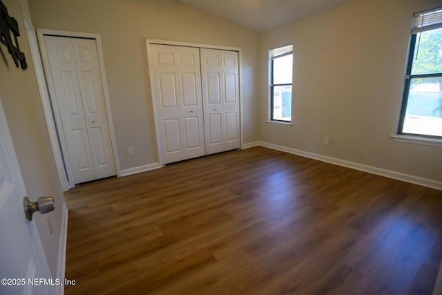 unfurnished bedroom with two closets, dark hardwood / wood-style floors, and lofted ceiling