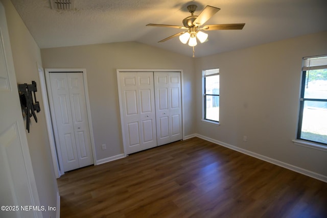 unfurnished bedroom featuring ceiling fan, lofted ceiling, dark wood-type flooring, and two closets