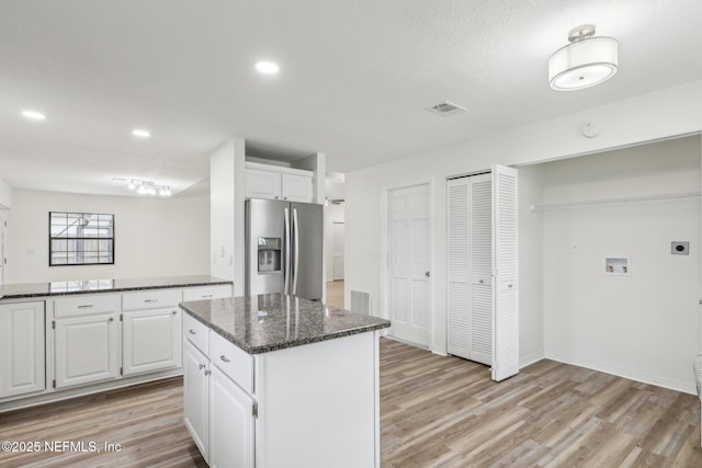 kitchen with stainless steel fridge, white cabinets, a center island, dark stone countertops, and light hardwood / wood-style floors