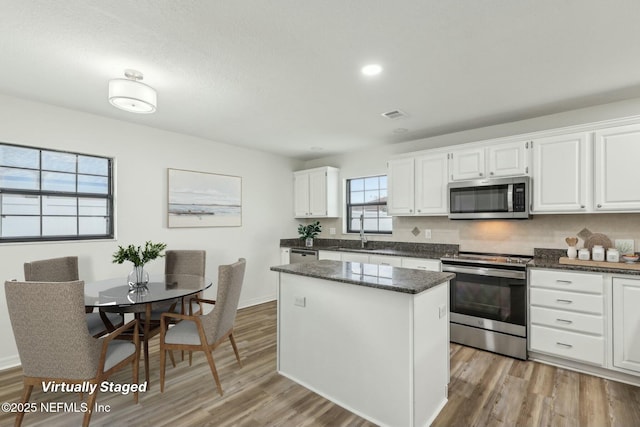 kitchen with light wood-type flooring, white cabinetry, tasteful backsplash, a kitchen island, and stainless steel appliances