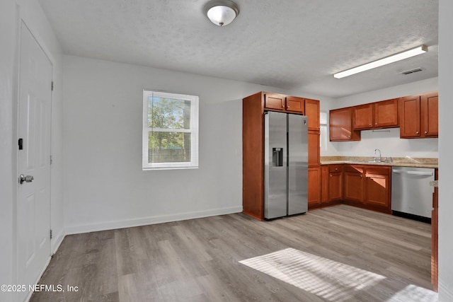 kitchen featuring sink, a textured ceiling, appliances with stainless steel finishes, and light hardwood / wood-style flooring