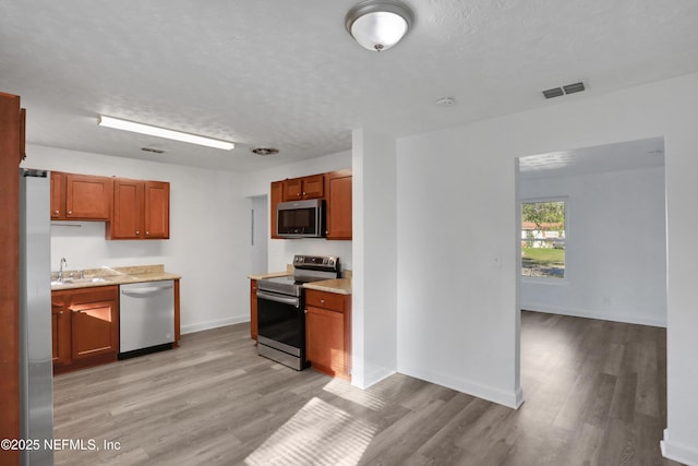 kitchen featuring sink, a textured ceiling, stainless steel appliances, and light wood-type flooring