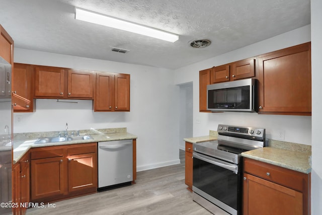 kitchen with appliances with stainless steel finishes, sink, a textured ceiling, and light hardwood / wood-style flooring