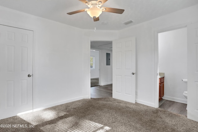 unfurnished bedroom with ceiling fan, dark carpet, ensuite bathroom, and electric panel