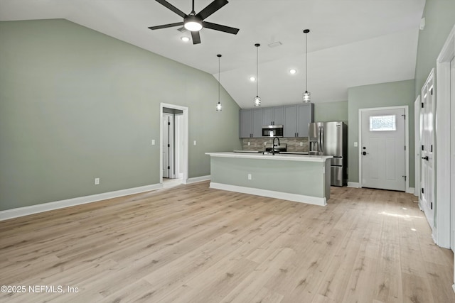 kitchen with gray cabinets, appliances with stainless steel finishes, decorative backsplash, a center island with sink, and light wood-type flooring