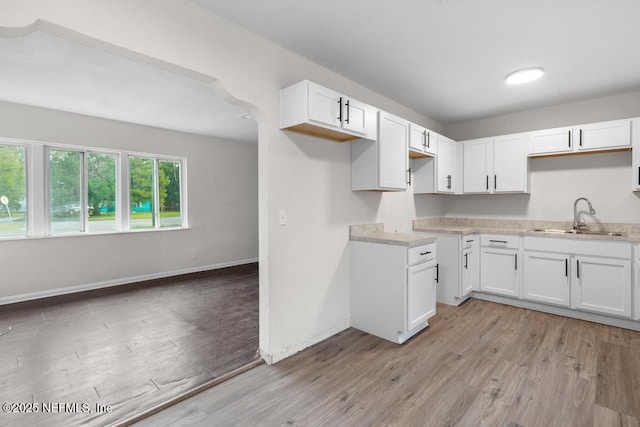 kitchen with light wood-type flooring, white cabinetry, and sink