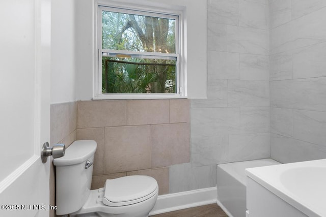 bathroom featuring a tub to relax in, tile walls, and toilet