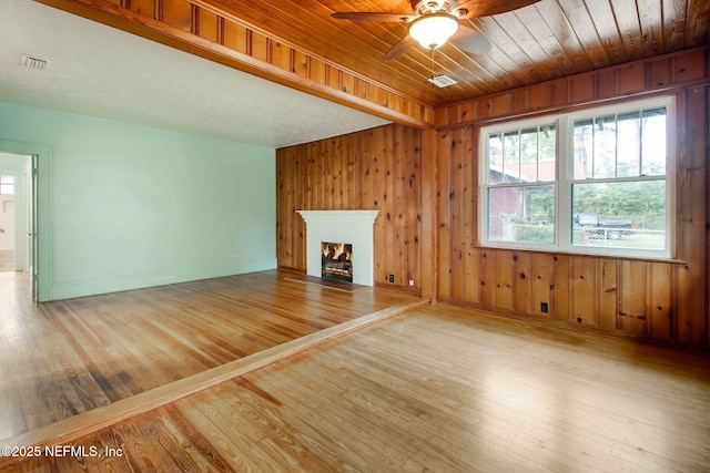 unfurnished living room with light wood-type flooring, wood ceiling, ceiling fan, a fireplace, and wood walls