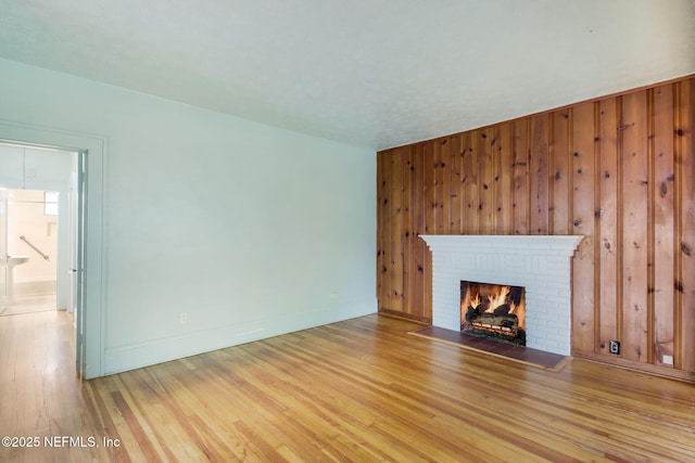 unfurnished living room featuring a fireplace, light hardwood / wood-style floors, and wooden walls