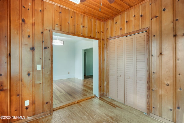 unfurnished bedroom featuring wood walls, light hardwood / wood-style floors, wooden ceiling, and a closet