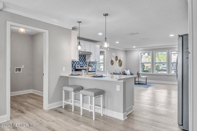 kitchen with kitchen peninsula, decorative light fixtures, backsplash, a breakfast bar area, and white cabinets