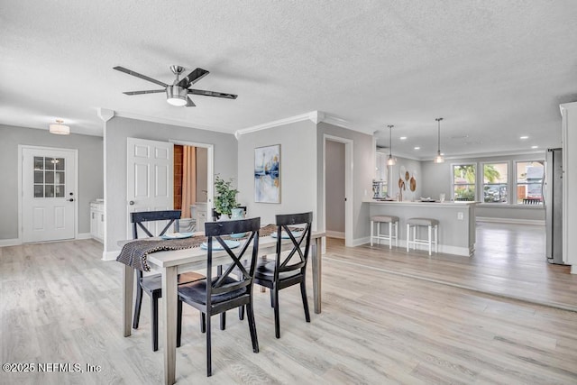 dining room with a textured ceiling, ceiling fan, light wood-type flooring, and crown molding